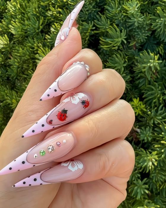 Pink polka-dot stiletto French tips with ladybug, flower and rhinestone accents